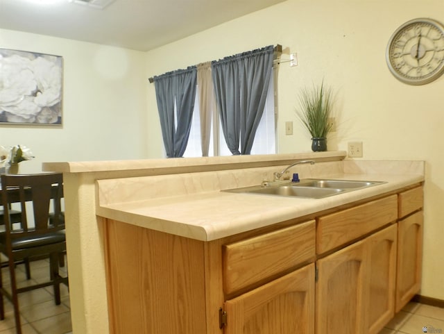 kitchen with a sink, a peninsula, light tile patterned floors, and light countertops
