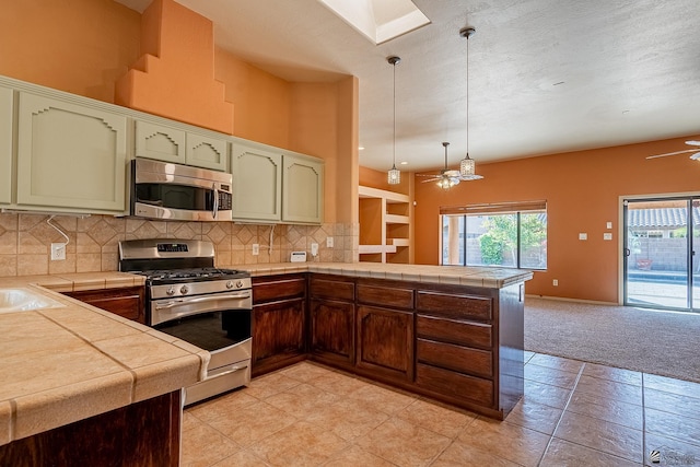 kitchen featuring ceiling fan, stainless steel appliances, kitchen peninsula, decorative light fixtures, and light carpet