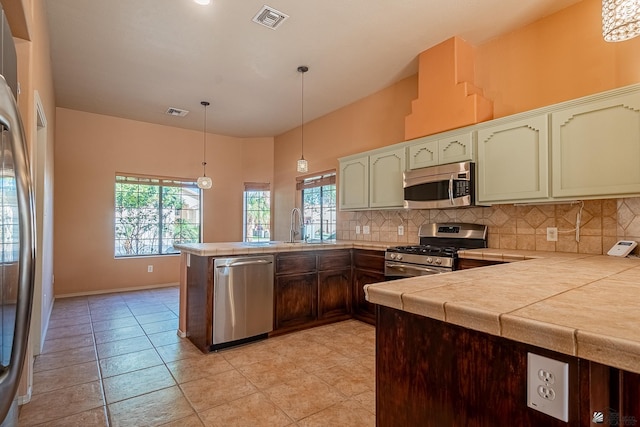 kitchen featuring hanging light fixtures, stainless steel appliances, tasteful backsplash, kitchen peninsula, and green cabinetry