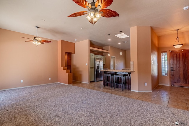 kitchen featuring kitchen peninsula, a kitchen breakfast bar, light tile patterned floors, stainless steel fridge with ice dispenser, and hanging light fixtures