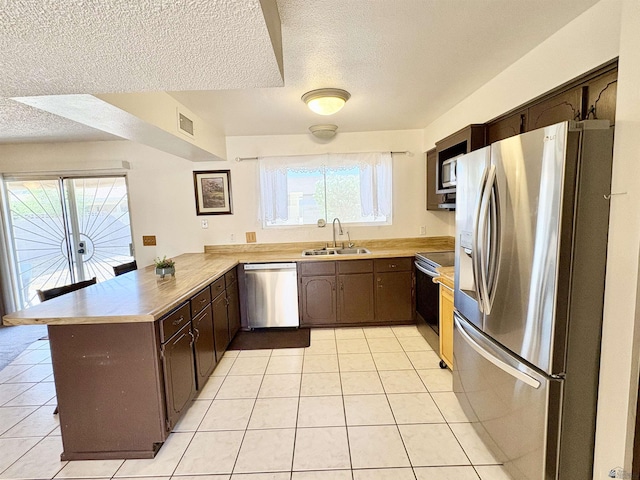 4447 W 14th Pl, Yuma, AZ 85364 - kitchen with appliances with stainless steel finishes, a peninsula, light tile patterned floors, a textured ceiling, and dark brown cabinets
