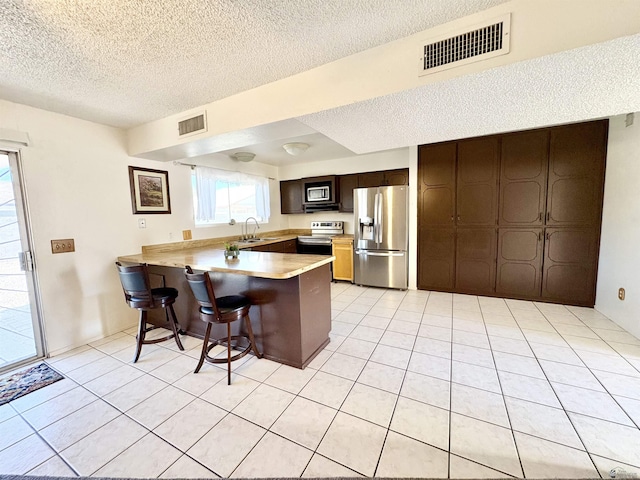 4447 W 14th Pl, Yuma, AZ 85364 - kitchen with stainless steel appliances, a textured ceiling, a peninsula, light countertops, and light tile patterned floors