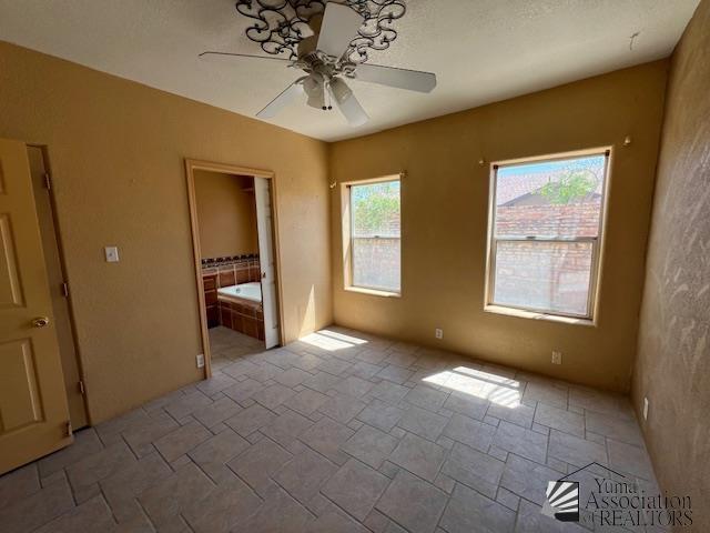 13257 E 55th Dr, Yuma, AZ 85367 - unfurnished bedroom featuring stone finish floor, ensuite bathroom, and a ceiling fan