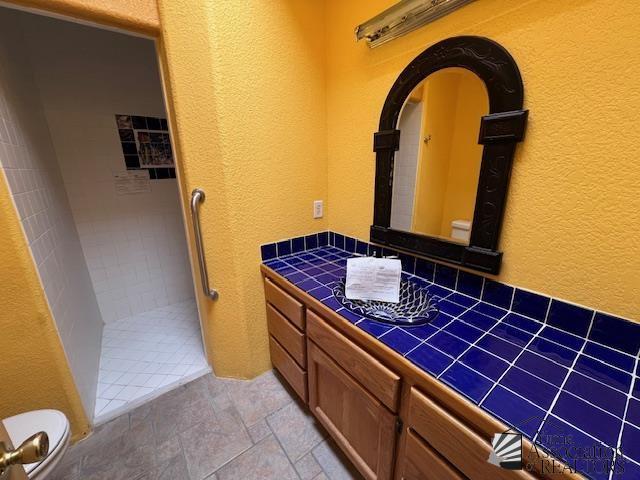 13257 E 55th Dr, Yuma, AZ 85367 - full bathroom featuring stone finish floor, vanity, toilet, a textured wall, and tiled shower