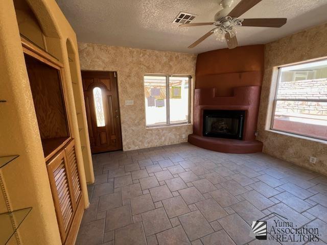 13257 E 55th Dr, Yuma, AZ 85367 - unfurnished living room with visible vents, a fireplace, ceiling fan, a textured ceiling, and stone finish flooring
