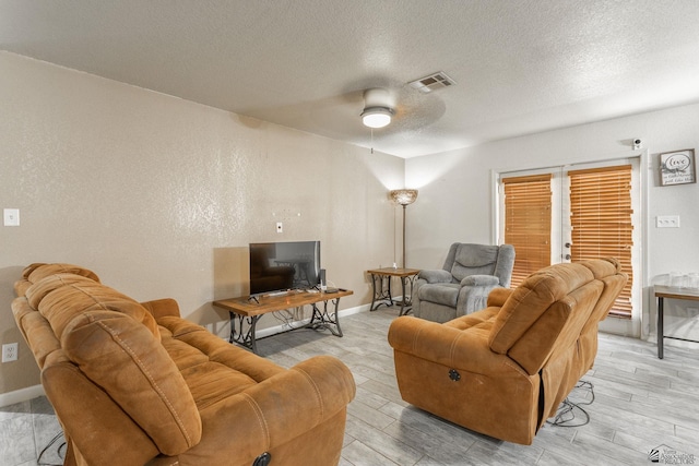 living room featuring ceiling fan, a textured ceiling, baseboards, light wood-type flooring, and visible vents