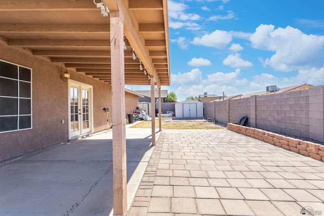 view of patio featuring a storage unit, a fenced backyard, an outbuilding, and french doors