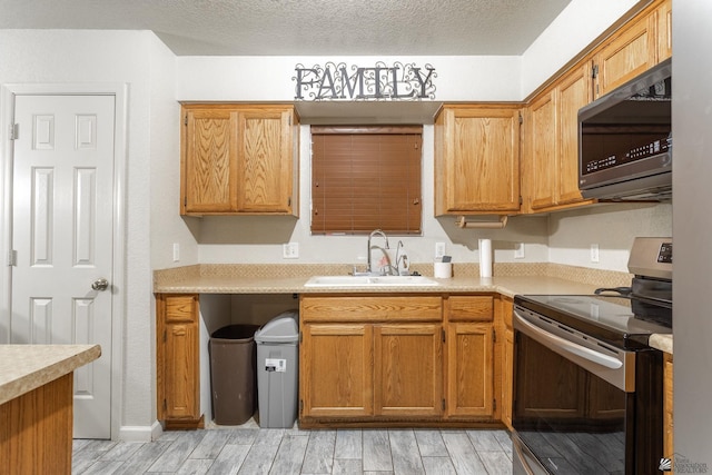 kitchen with electric range, a sink, light countertops, brown cabinetry, and light wood-type flooring