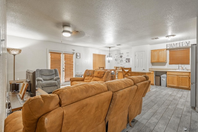 living room featuring ceiling fan, a textured ceiling, visible vents, and wood finished floors