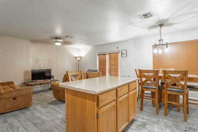 kitchen with wood tiled floor, a textured ceiling, visible vents, light countertops, and open floor plan