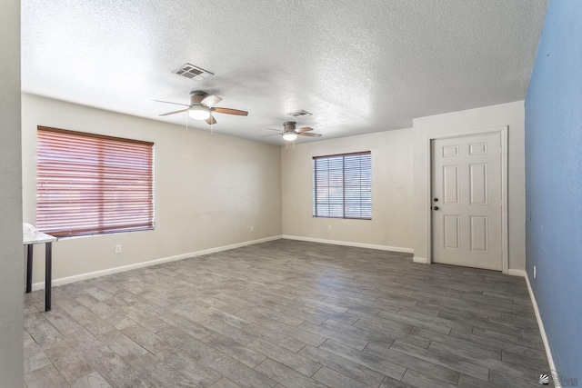 spare room with a textured ceiling, a ceiling fan, baseboards, wood finished floors, and visible vents