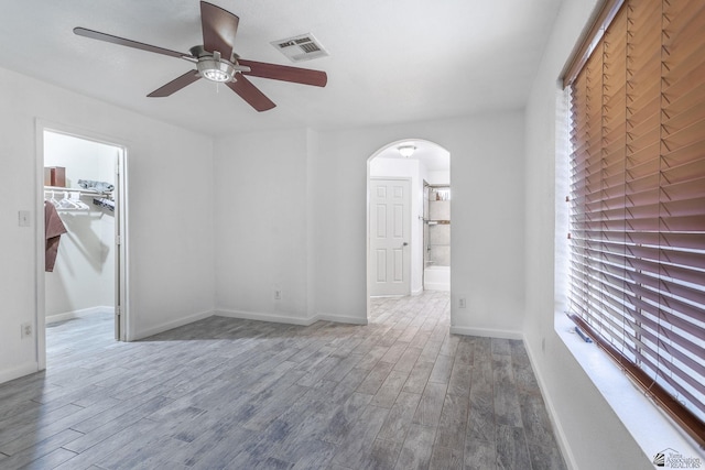 interior space with a walk in closet, visible vents, arched walkways, wood finished floors, and baseboards