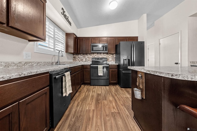 4841 W 10th Pl, Yuma, AZ 85364 - kitchen with black appliances, light wood-style floors, dark brown cabinetry, vaulted ceiling, and decorative backsplash