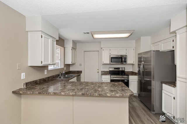 2928 W 27th Pl, Yuma, AZ 85364 - kitchen with stainless steel appliances, dark countertops, a peninsula, dark wood-style flooring, and white cabinetry