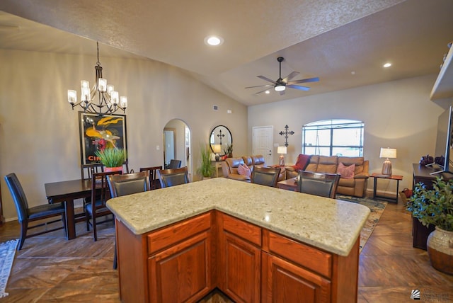 kitchen with lofted ceiling, ceiling fan with notable chandelier, light stone countertops, a kitchen island, and decorative light fixtures