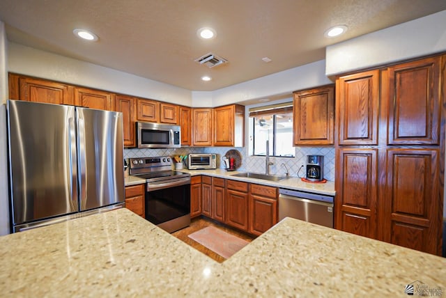 kitchen with light stone counters, sink, decorative backsplash, and appliances with stainless steel finishes