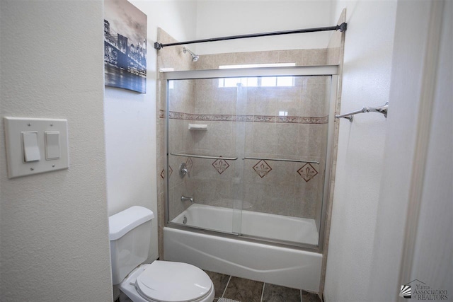 full bathroom featuring a textured wall, toilet, and shower / bath combination with glass door