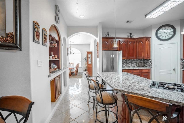 kitchen featuring visible vents, light stone countertops, a kitchen bar, appliances with stainless steel finishes, and hanging light fixtures