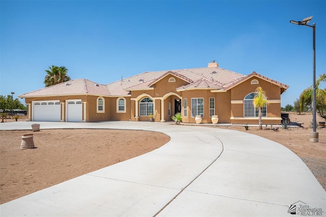 mediterranean / spanish home with curved driveway, stucco siding, a chimney, a tiled roof, and an attached garage