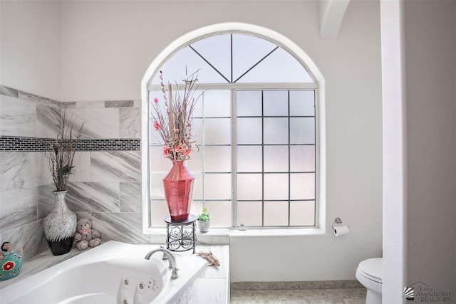 bathroom with toilet and a tub with jets