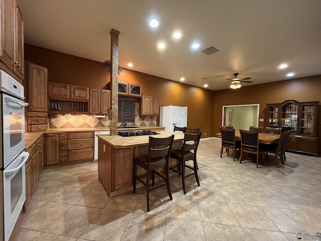 kitchen with a center island, white appliances, decorative backsplash, ceiling fan, and light tile patterned floors