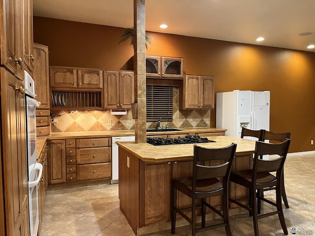 kitchen featuring tasteful backsplash, white appliances, a kitchen island, a breakfast bar area, and light tile patterned flooring