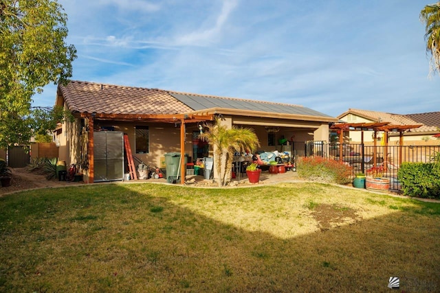 rear view of house featuring fence, stucco siding, a yard, a tile roof, and solar panels