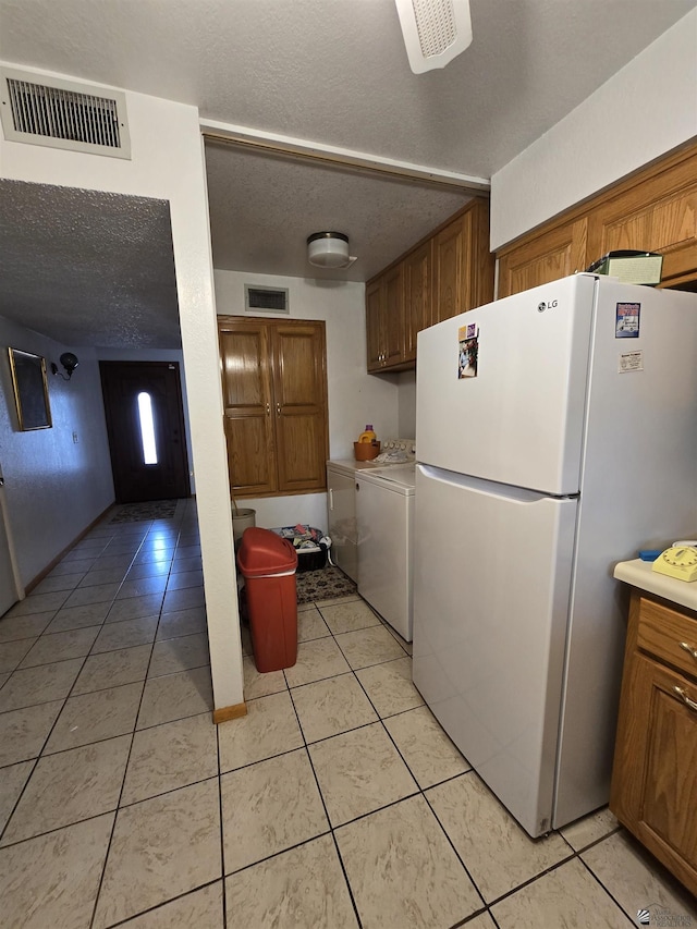 kitchen with visible vents, brown cabinetry, a textured ceiling, and freestanding refrigerator