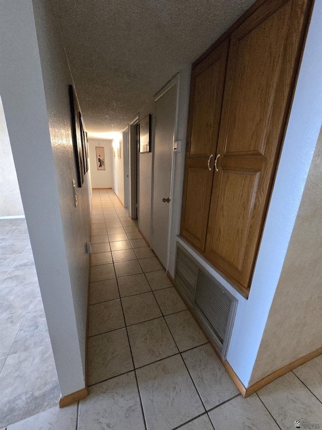 hall featuring a textured ceiling, light tile patterned flooring, visible vents, and baseboards