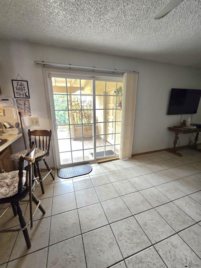 doorway to outside with a textured ceiling, light tile patterned flooring, and baseboards