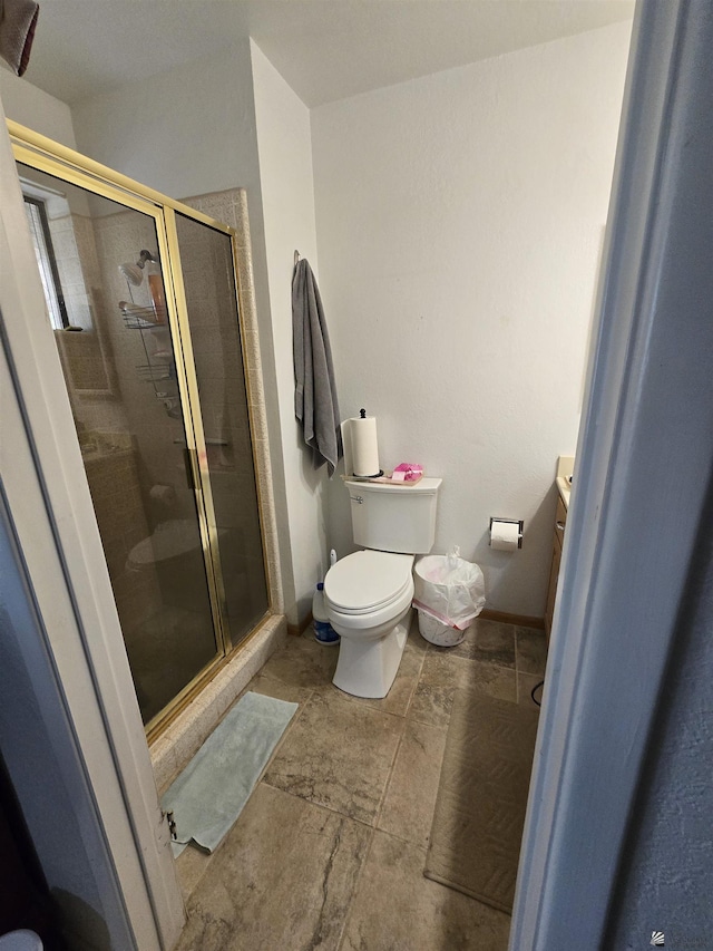 bathroom featuring stone finish floor, a shower stall, toilet, and vanity