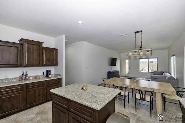 4272 W 27th Pl, Yuma, AZ 85364 - kitchen with dark brown cabinets, light stone countertops, a center island, open floor plan, and visible vents