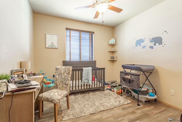 bedroom featuring a crib, wood finished floors, baseboards, and ceiling fan