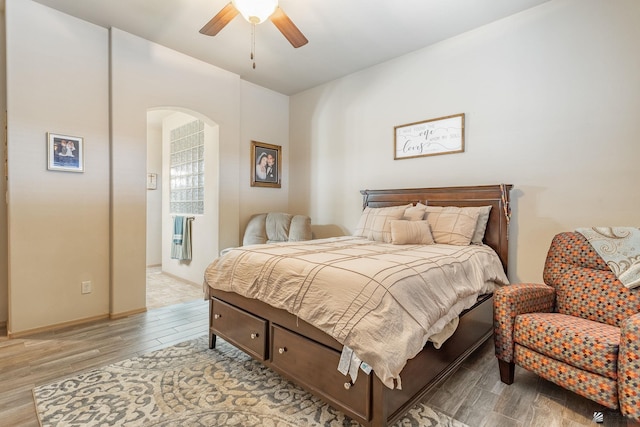 bedroom with light wood-type flooring, arched walkways, baseboards, and a ceiling fan