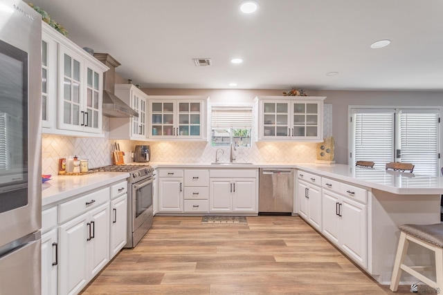 kitchen featuring white cabinets, sink, light hardwood / wood-style flooring, kitchen peninsula, and stainless steel appliances