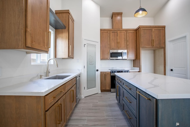 kitchen with brown cabinets, light stone counters, appliances with stainless steel finishes, a sink, and a center island