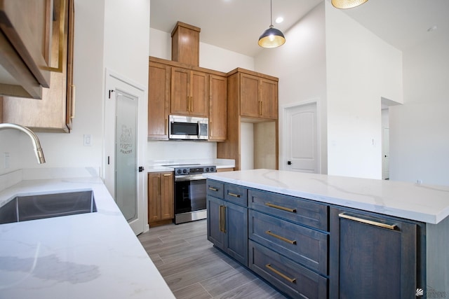 kitchen featuring a towering ceiling, light wood-style floors, light stone counters, a sink, and stainless steel appliances