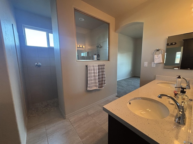 bathroom featuring a walk in shower, a sink, tile patterned flooring, double vanity, and baseboards
