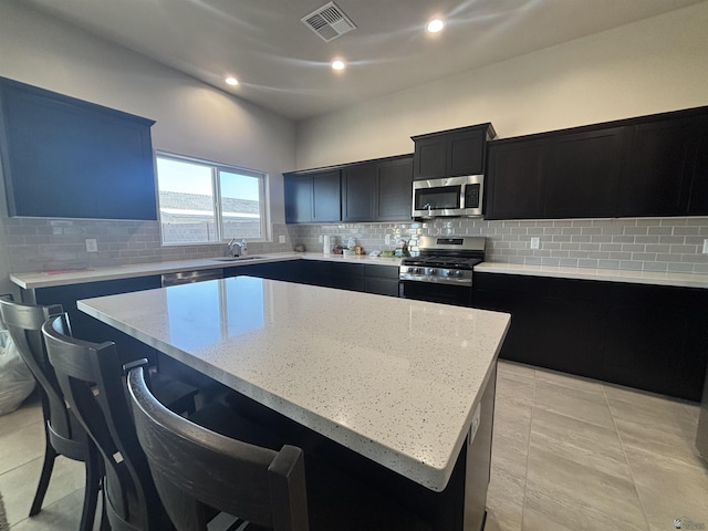kitchen with appliances with stainless steel finishes, dark cabinetry, a kitchen island, and visible vents
