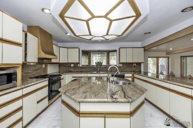 kitchen with custom range hood, a kitchen island with sink, sink, black gas stove, and white cabinetry