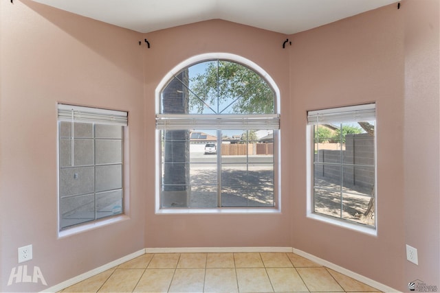 tiled empty room featuring baseboards and vaulted ceiling