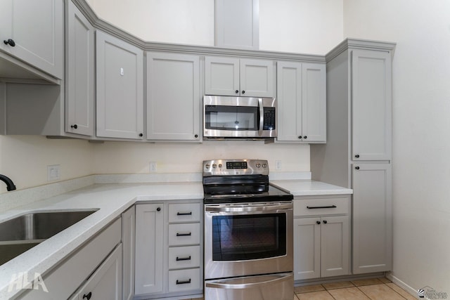 kitchen with stainless steel appliances, light tile patterned flooring, gray cabinetry, and a sink