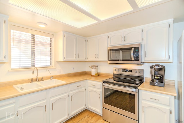 kitchen with white cabinets, appliances with stainless steel finishes, a sink, and light countertops