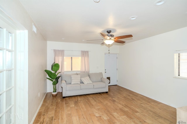 living room featuring ceiling fan, light wood finished floors, visible vents, and a wealth of natural light