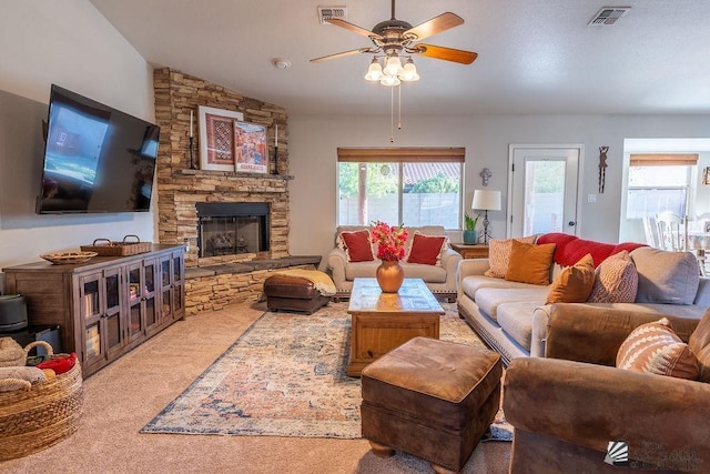 living room featuring carpet floors, ceiling fan, visible vents, and a stone fireplace