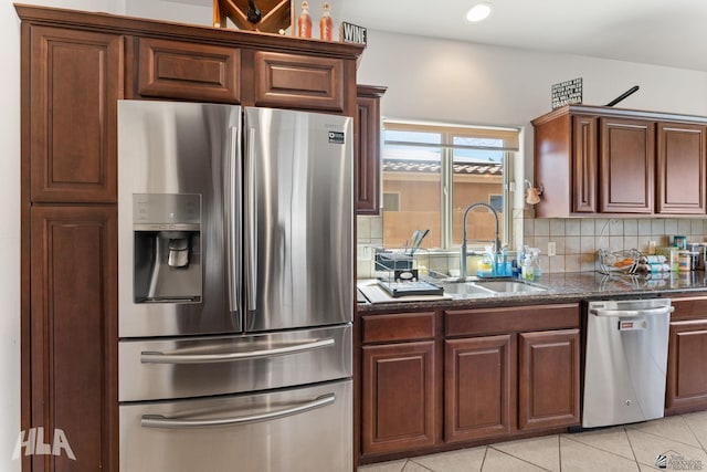 kitchen featuring backsplash, a sink, dark stone counters, stainless steel appliances, and light tile patterned flooring