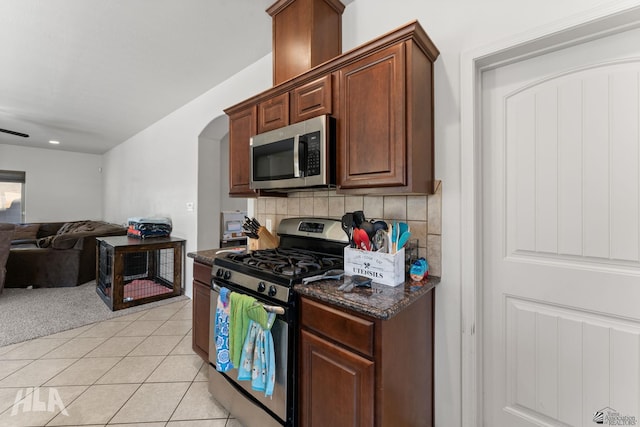 kitchen with appliances with stainless steel finishes, arched walkways, open floor plan, decorative backsplash, and light tile patterned floors