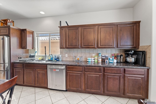 kitchen with a sink, dark stone countertops, backsplash, light tile patterned floors, and stainless steel appliances