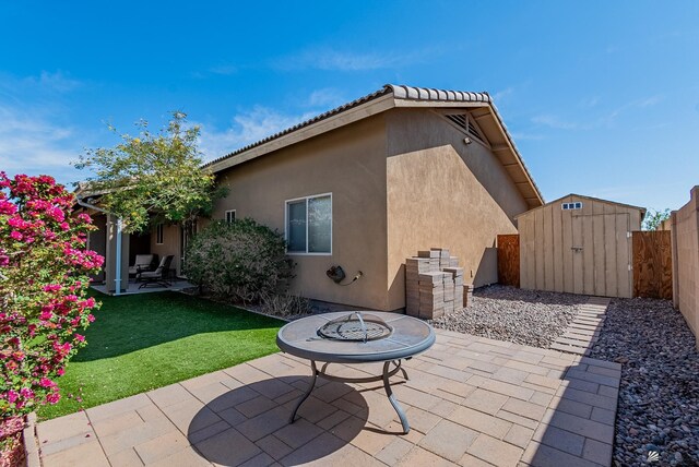 rear view of property featuring an outdoor structure, stucco siding, a shed, a fenced backyard, and a patio