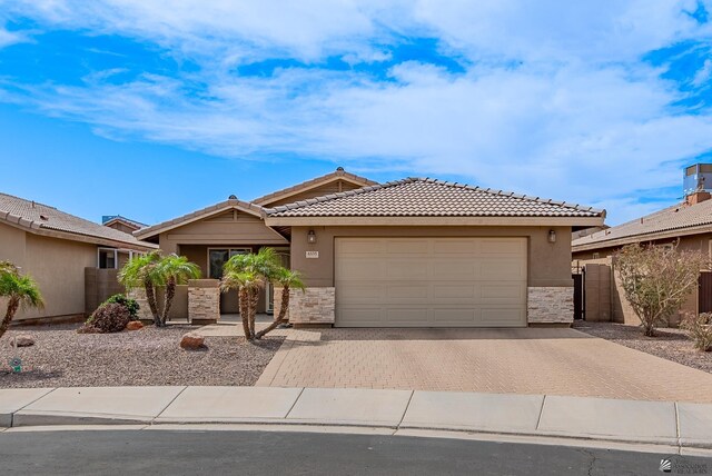 ranch-style home with a tiled roof, decorative driveway, stone siding, and a garage